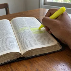 Mão marcando versículos com marca-texto amarelo na Bíblia
